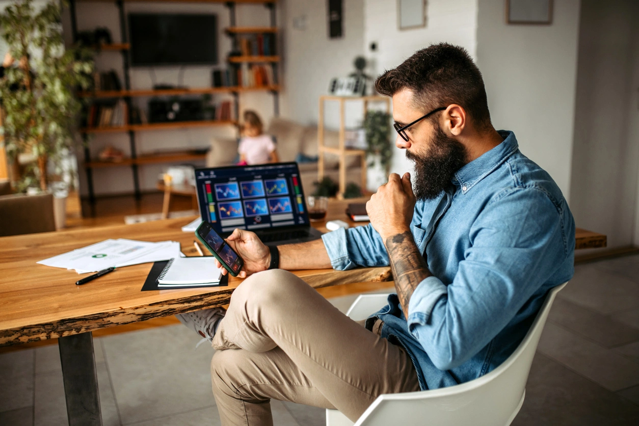 Should I Wait Until The Market Calms Down Before Investing Investor at home reviewing market charts on a laptop, deciding whether to invest now or wait during volatility.